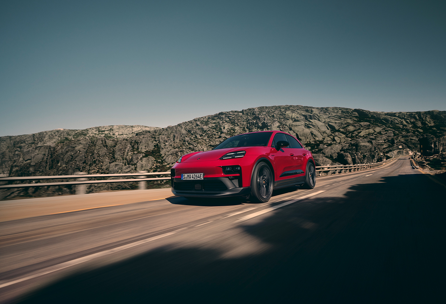 Un carrusel de imágenes muestra el Porsche Macan 2026 en Carmine Red y el Porsche Cayenne Electric en Mystic Green, ambos en la carretera. 