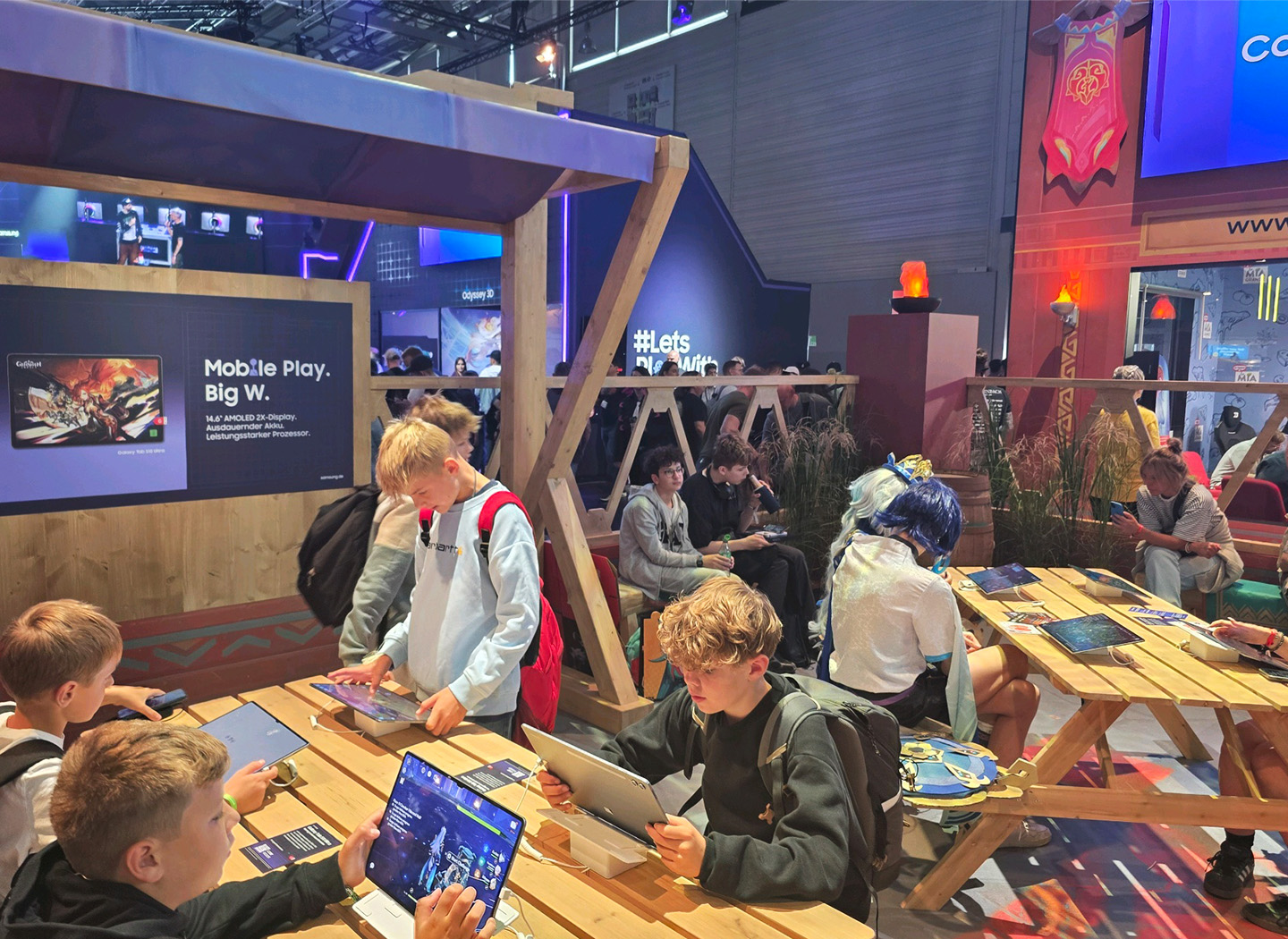 Visitors to the Samsung booth at Gamescom 2025 are trying out the Galaxy devices placed on the tables.